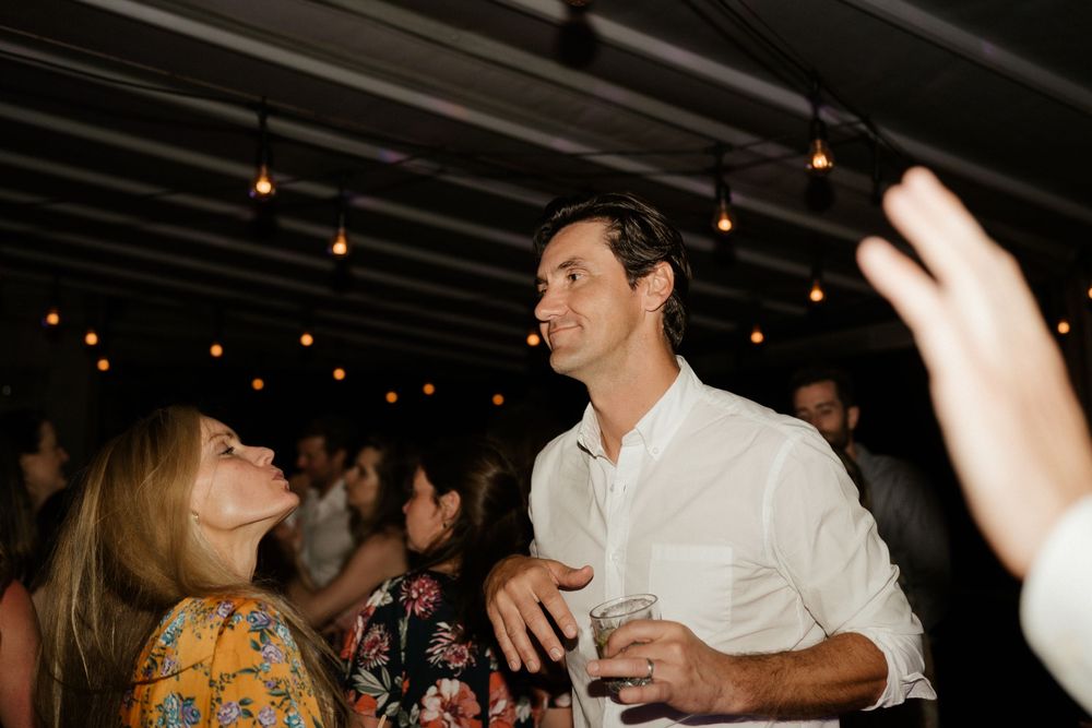 Party guests dancing and socializing under string lights at an indoor celebration.