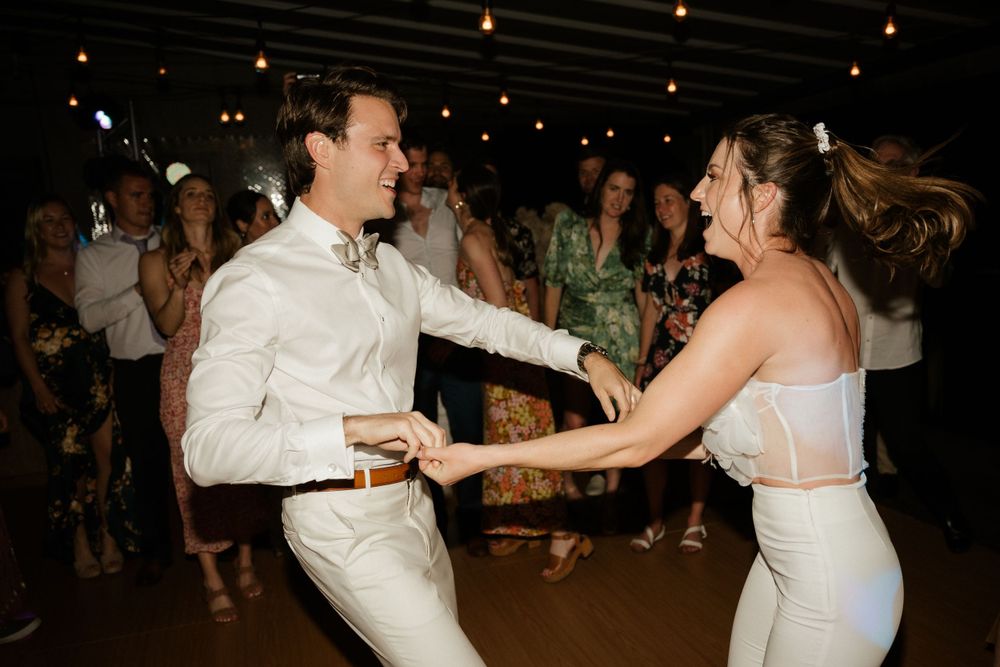 Energetic couple dancing together at a wedding reception under string lights.