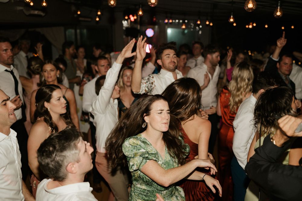 Crowded dance floor with partygoers dancing under string lights at a celebration.