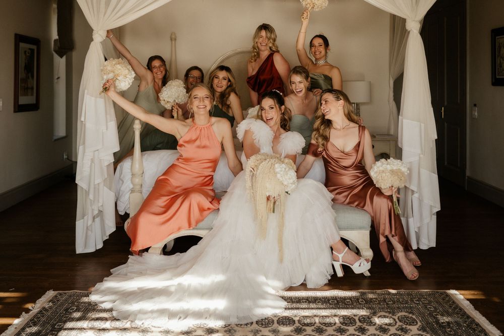 Wedding party in colorful dresses posing playfully on white canopy bed.
