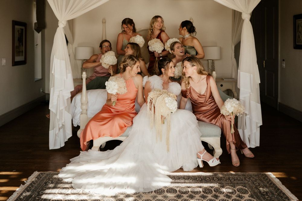 Wedding party gathers on draped canopy bed in soft natural light.