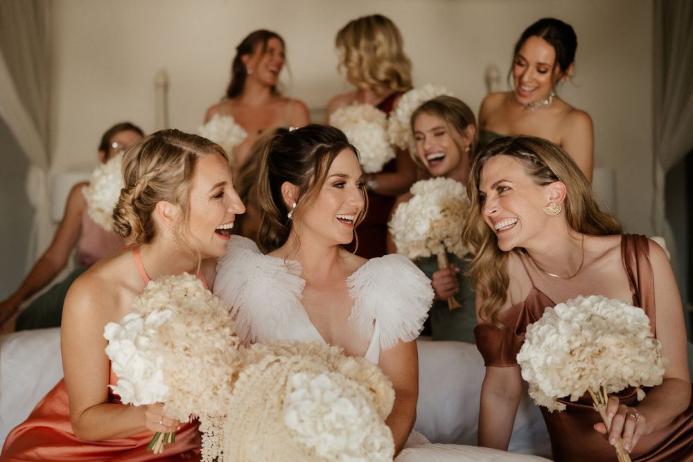 Bridesmaids sharing a candid moment while holding white bouquets.