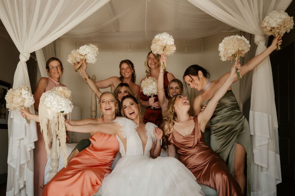 Bridal party celebrates joyfully under white draped canopy holding bouquets.