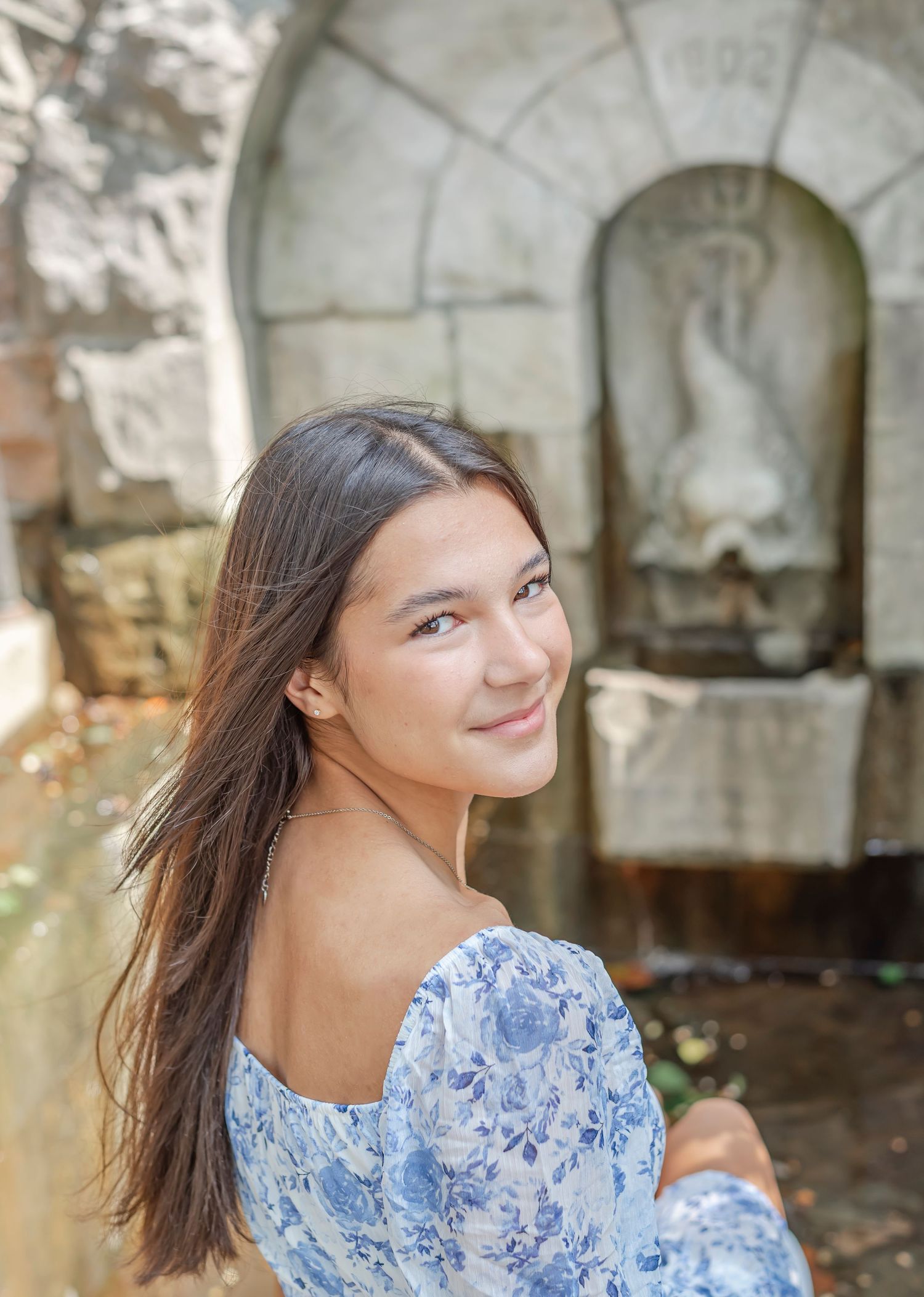 A blue floral dress stands out against an ornate stone fountain backdrop.