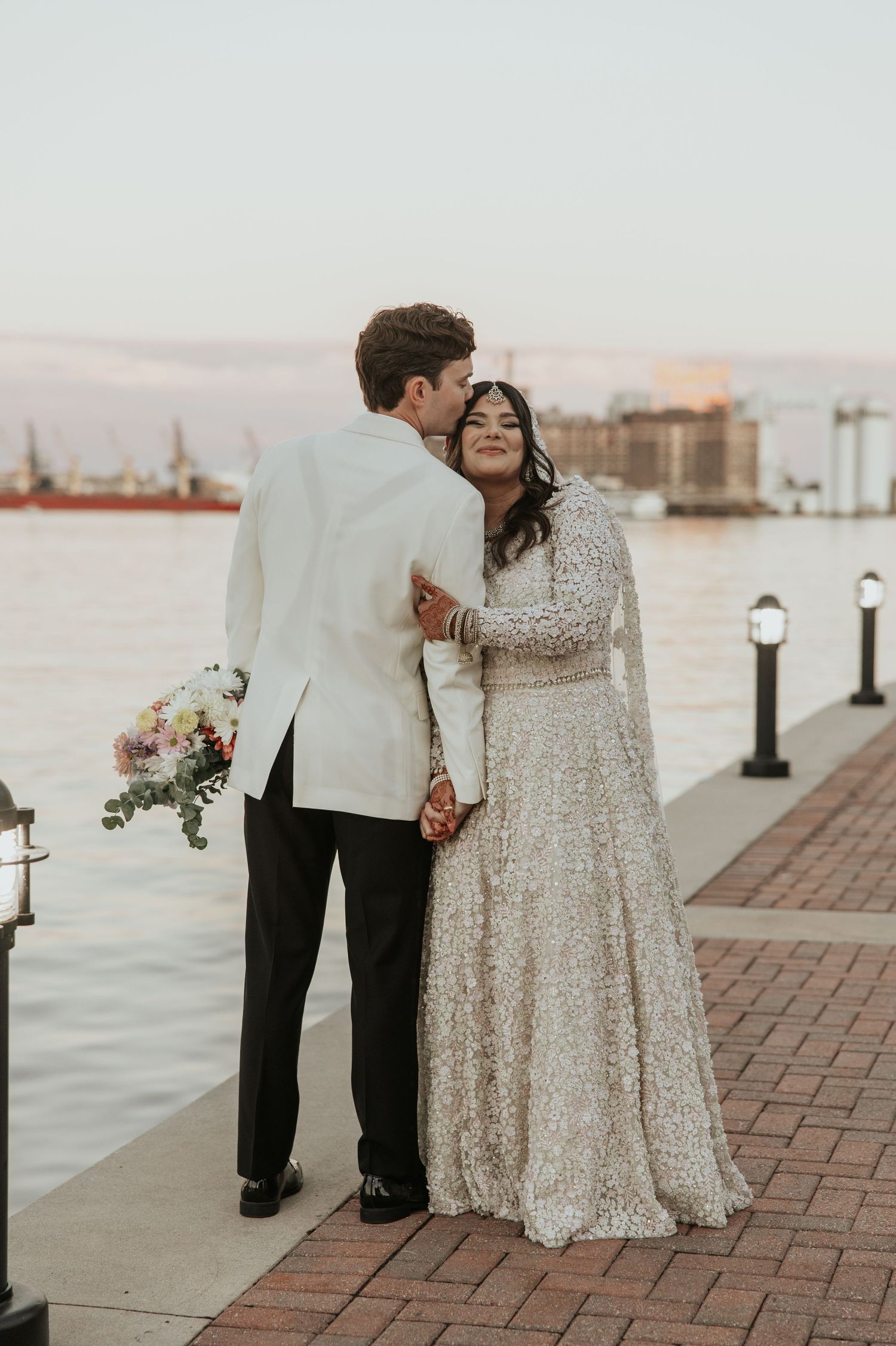 Romantic waterfront wedding portrait of couple in formal attire at sunset.