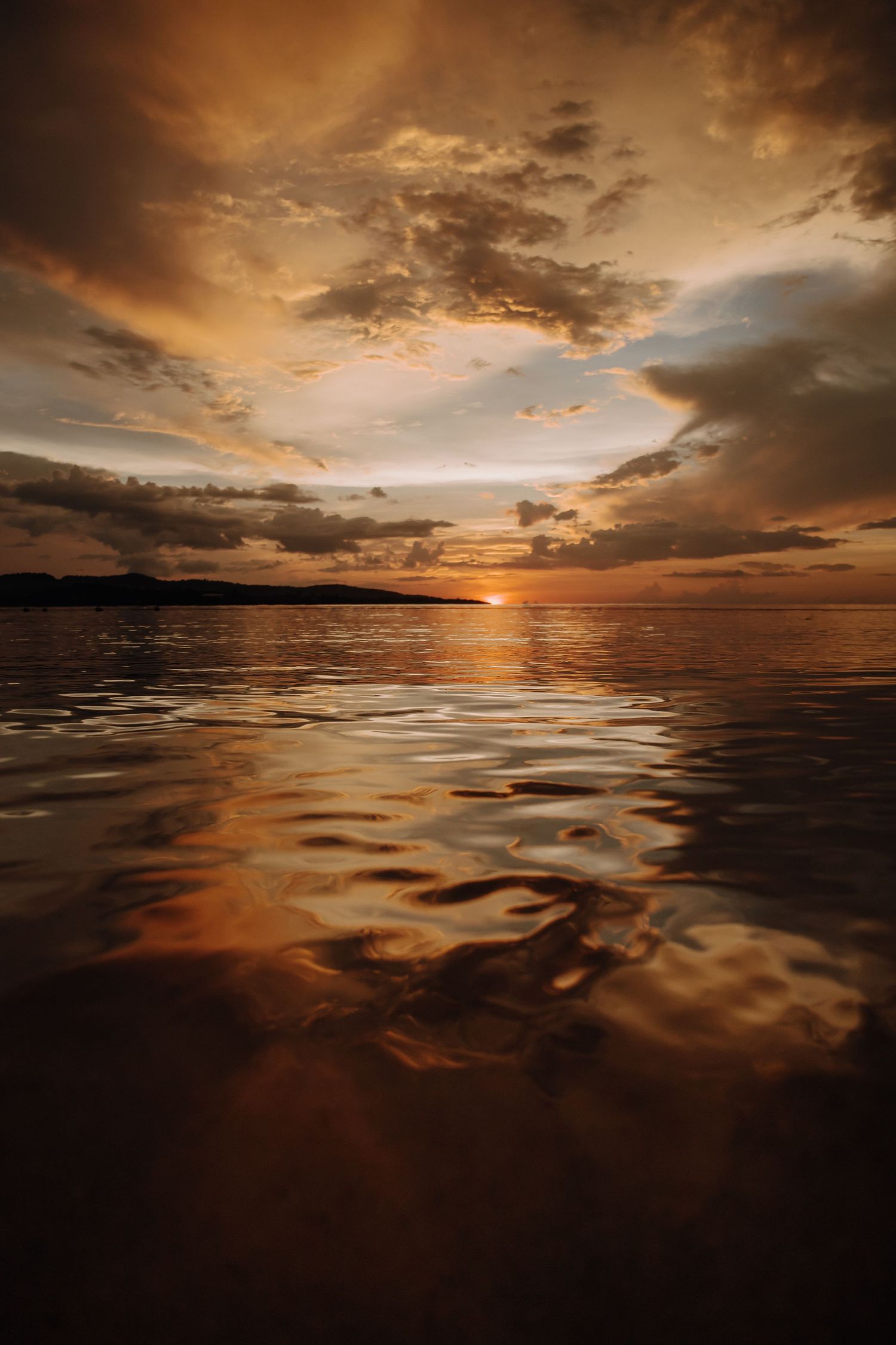 Dramatic orange sunset over calm waters with reflective clouds creating a mirror effect.