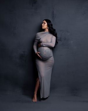 Elegant maternity portrait in fitted grey dress against dark backdrop.