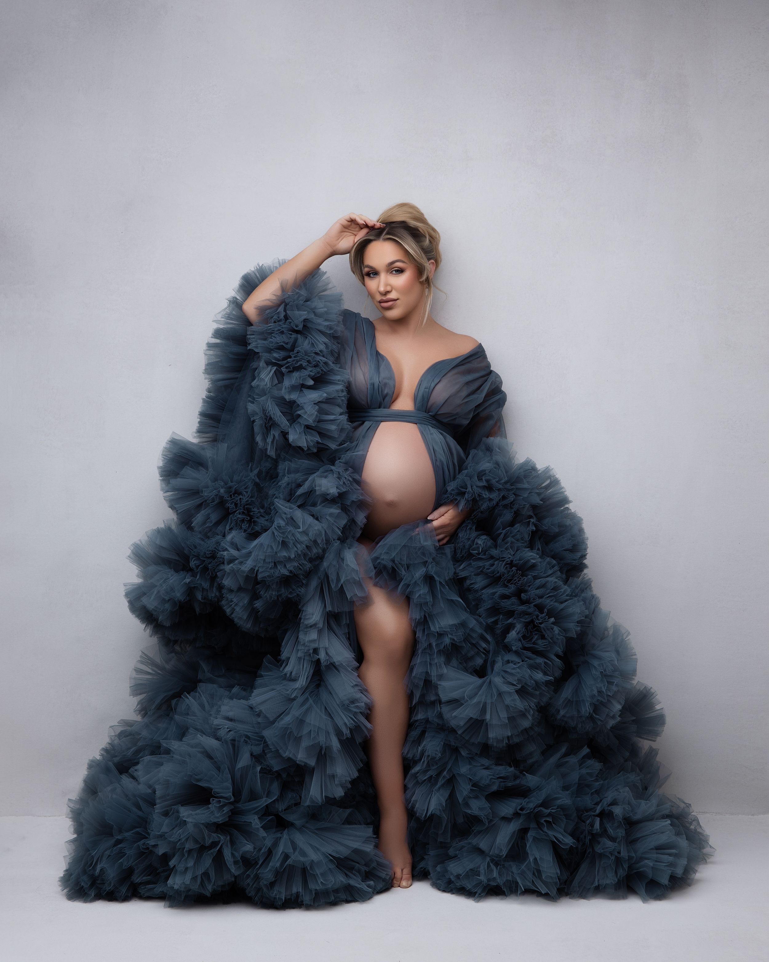 A dramatic navy blue tulle gown with voluminous ruffles cascades elegantly against a light gray backdrop.