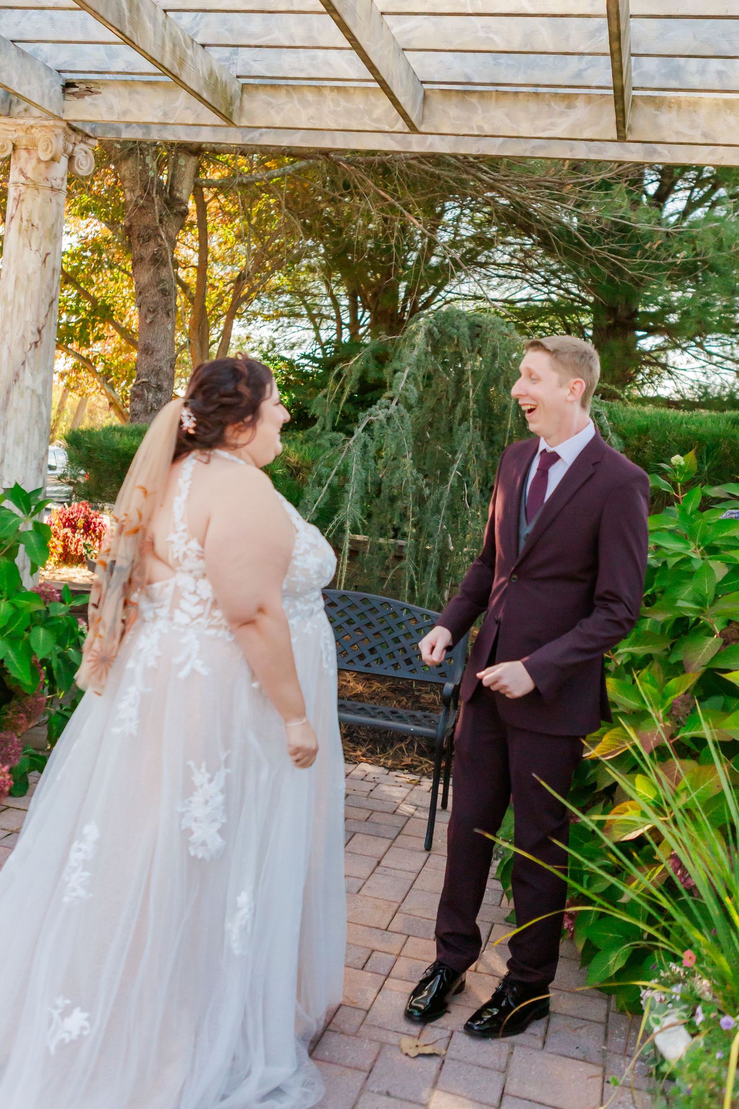 Couple sharing first look moment under garden pergola surrounded by greenery.