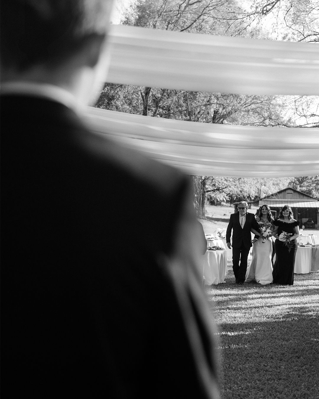 Black and white wedding ceremony scene with guests viewed through architectural elements.
