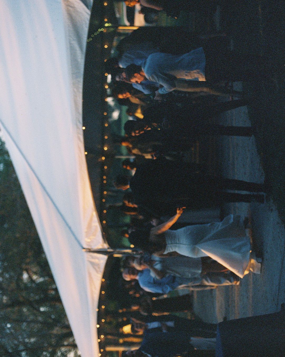 Wedding reception under a tent with string lights and dancing guests.