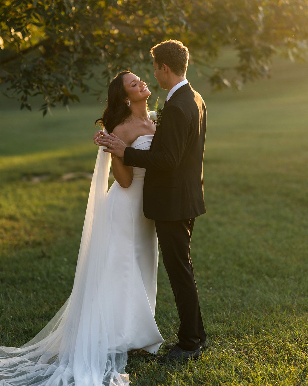 Sunset wedding photos on a grassy hill with flowing white dress and veil.