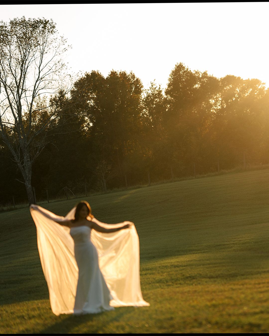 Dramatic silhouette of bride's dress and veil backlit by golden sunset.