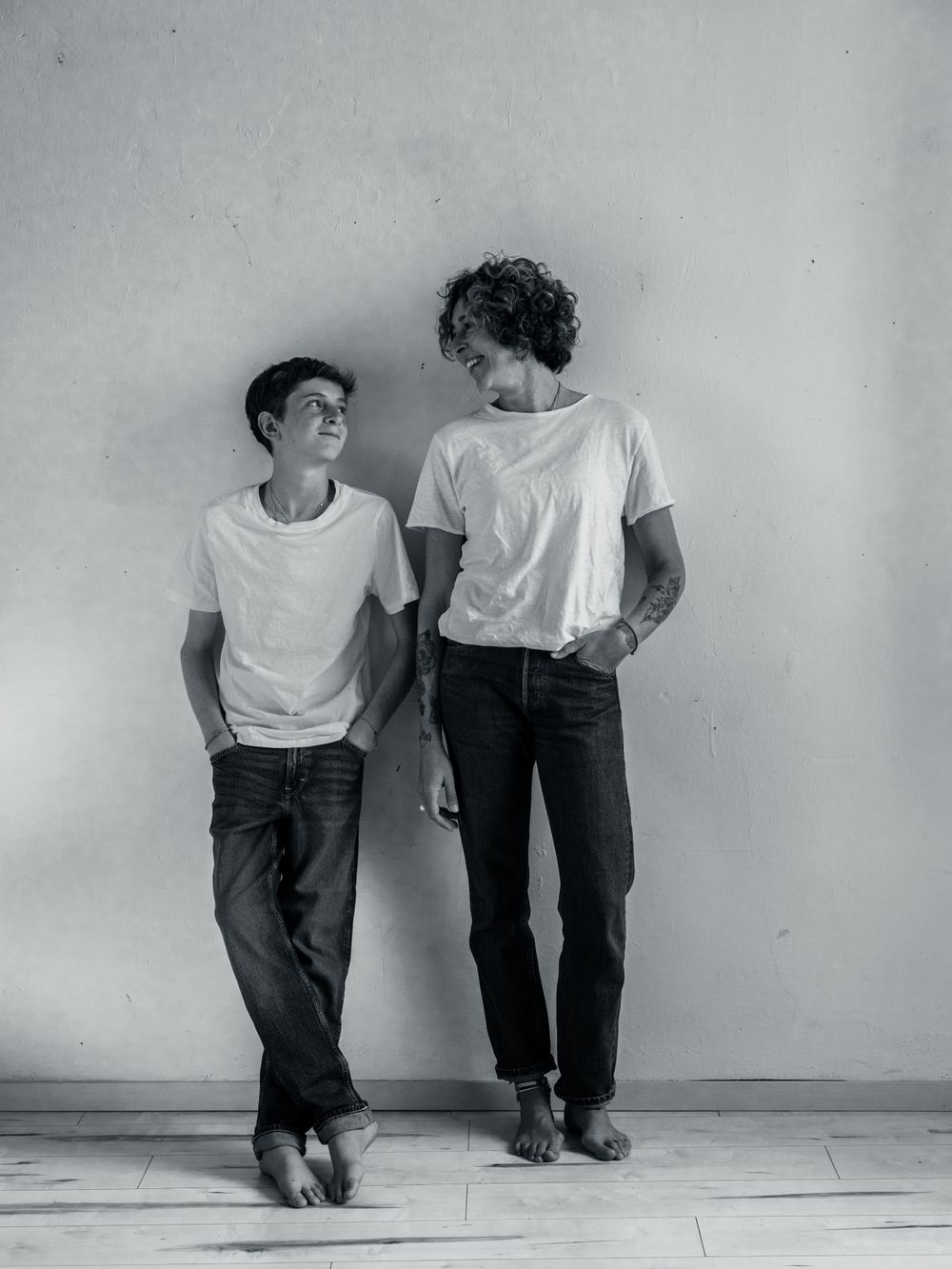 Two people in white shirts and dark pants leaning against a wall in various poses.