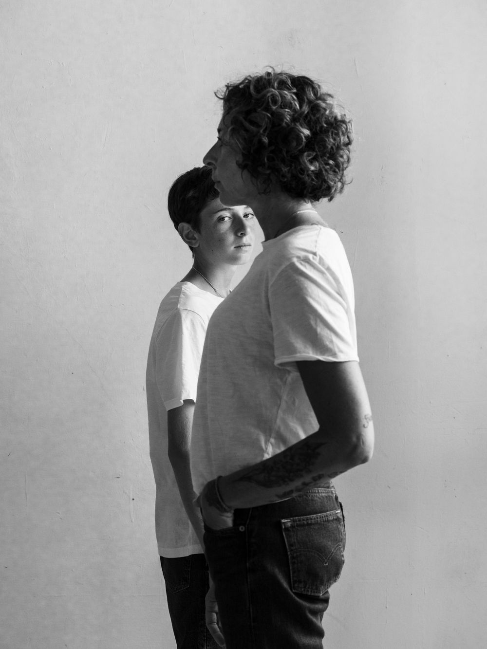Two people in white shirts and dark pants posing against a light background.