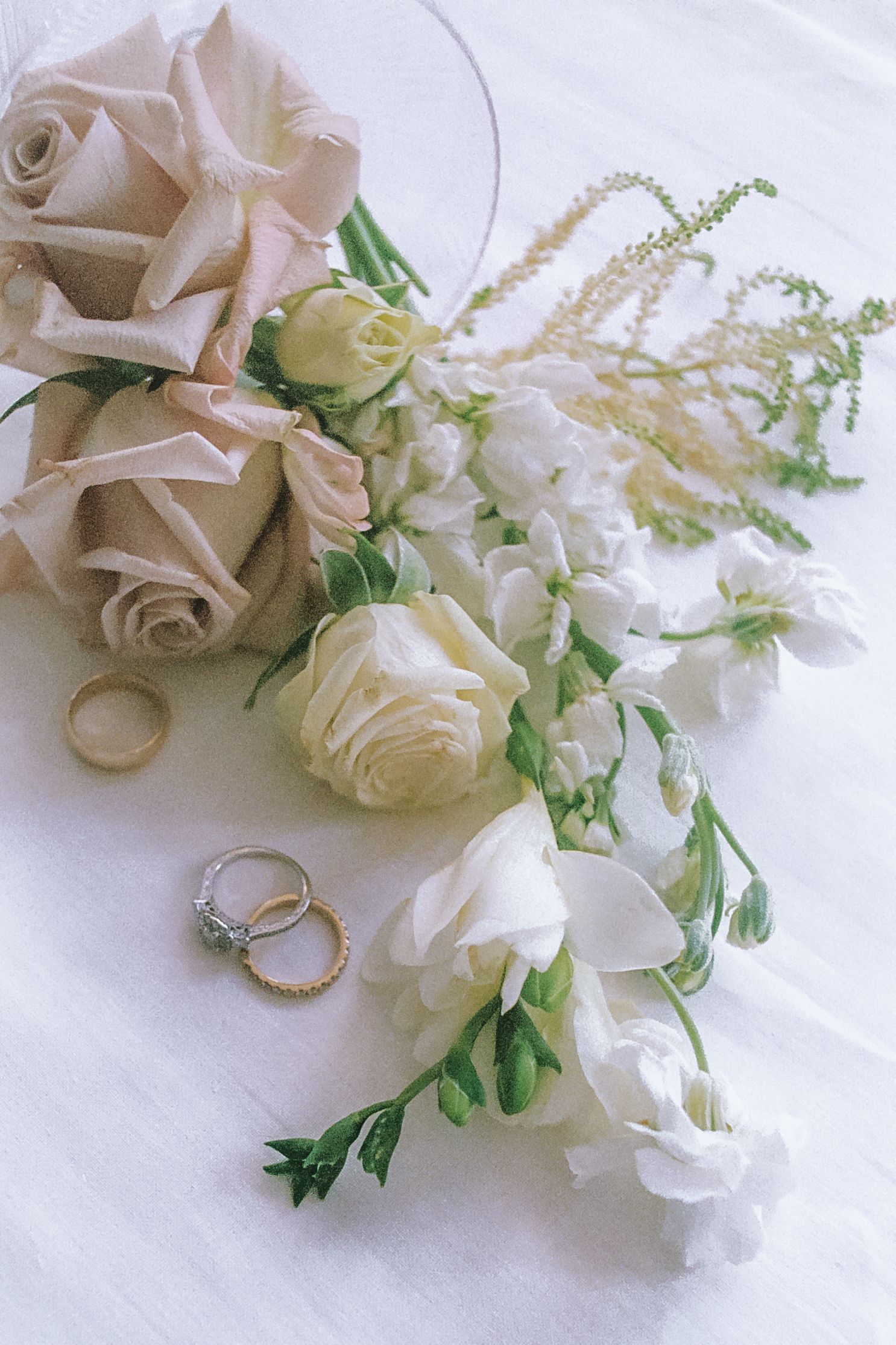 Delicate white roses and wedding rings arranged on a light fabric background.