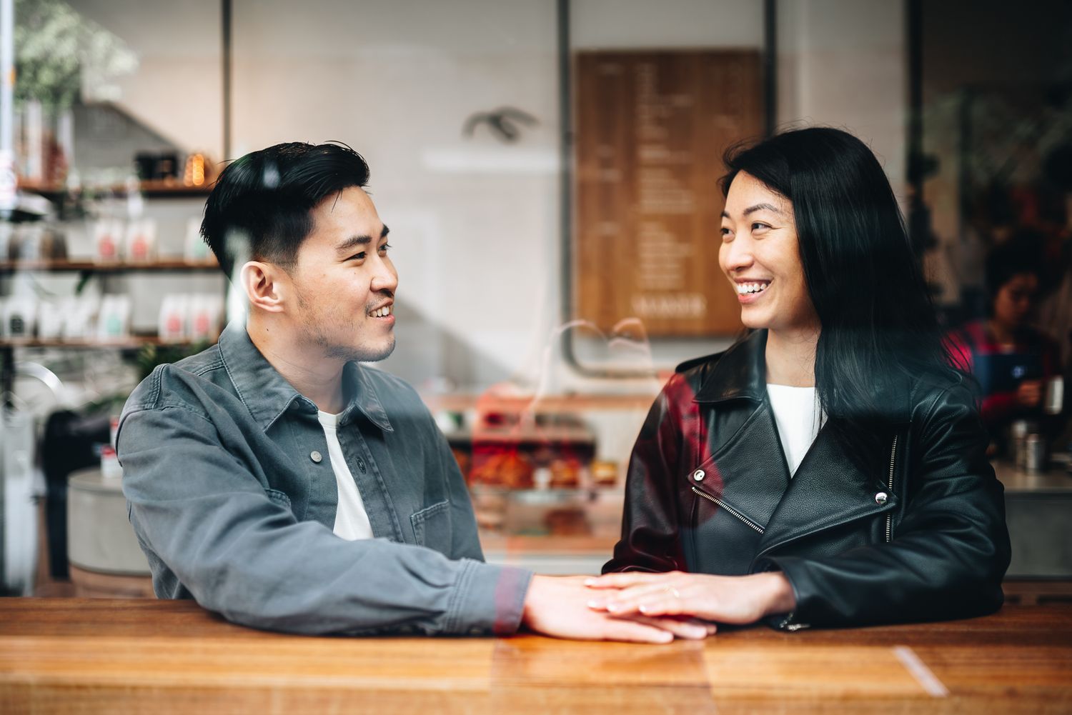 Asian couple shares a joyful conversation at a cozy coffee shop taken by Melbourne casual couples and engagement photographer