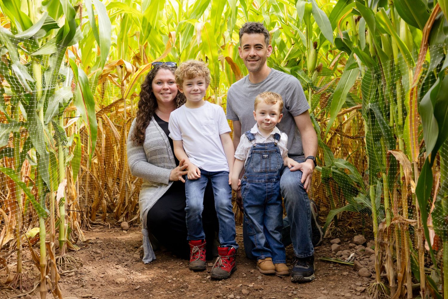 Happy family poses together in front of tall corn stalks on a bright sunny day.
