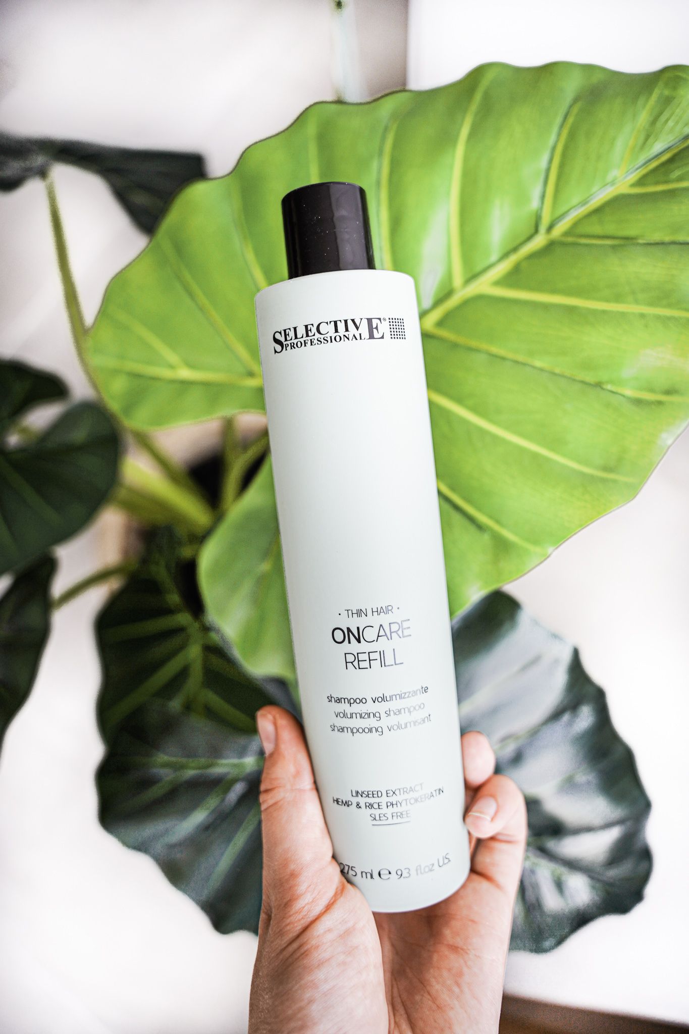 White Selective hair product bottle held against large green tropical leaf background.