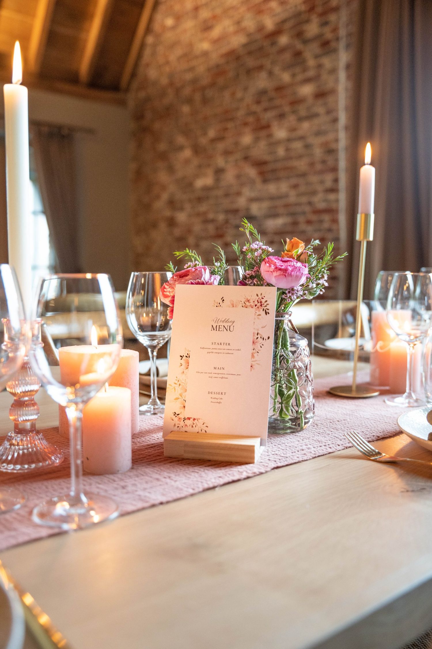 Romantic table setting with pink menu card, lit candles and fresh flower arrangements.