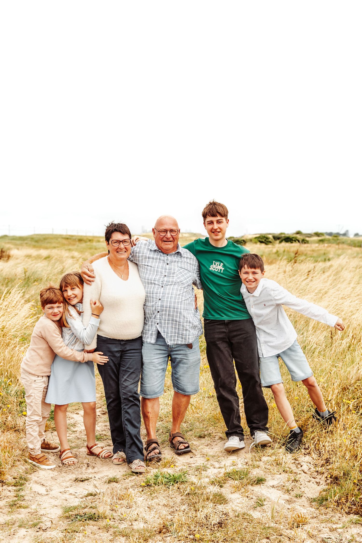 A multi-generational family poses together in a grassy field on a sunny day.