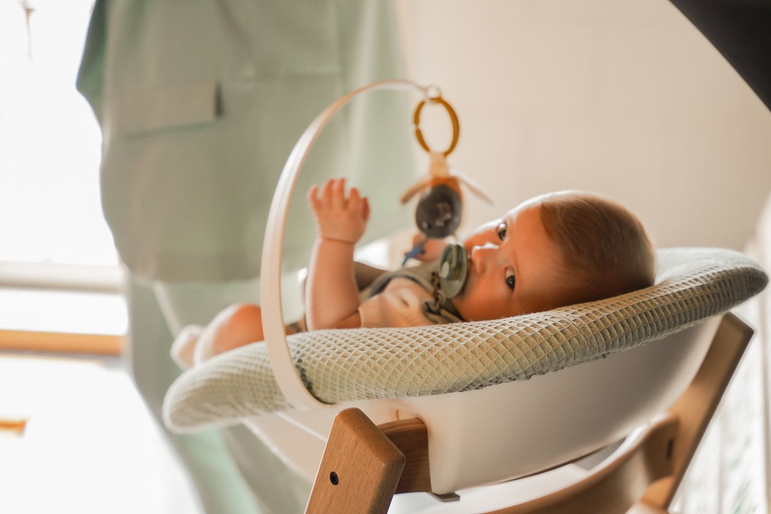 Small child reaching for toy while sitting in modern white baby seat.
