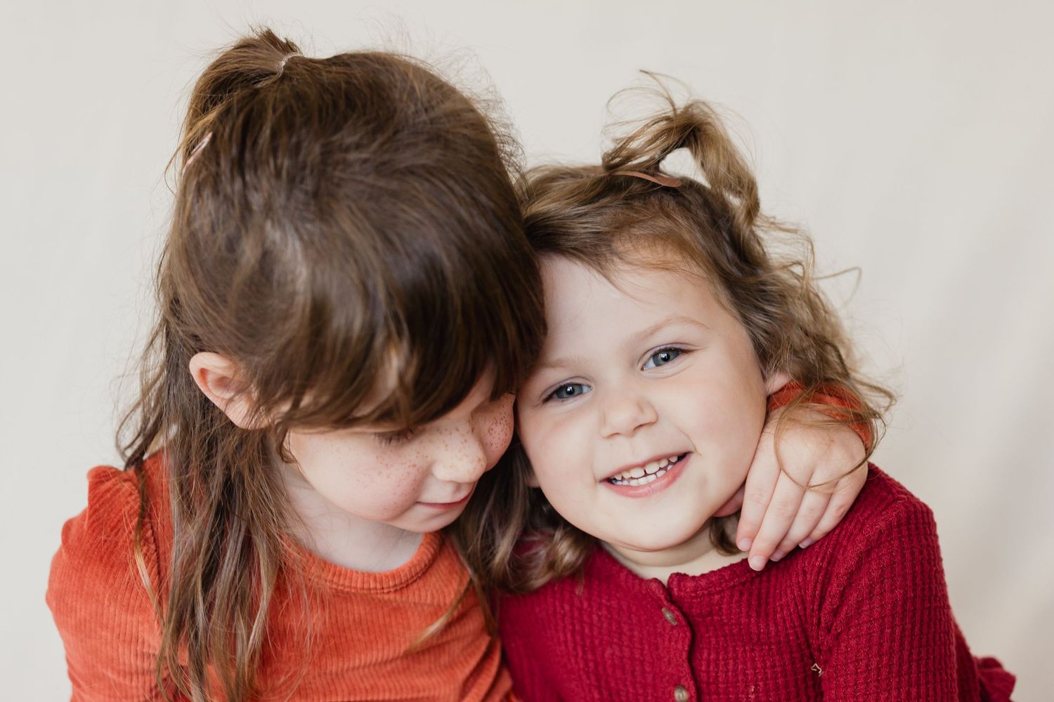 Two people sharing a warm embrace and laughing together in red and orange sweaters.