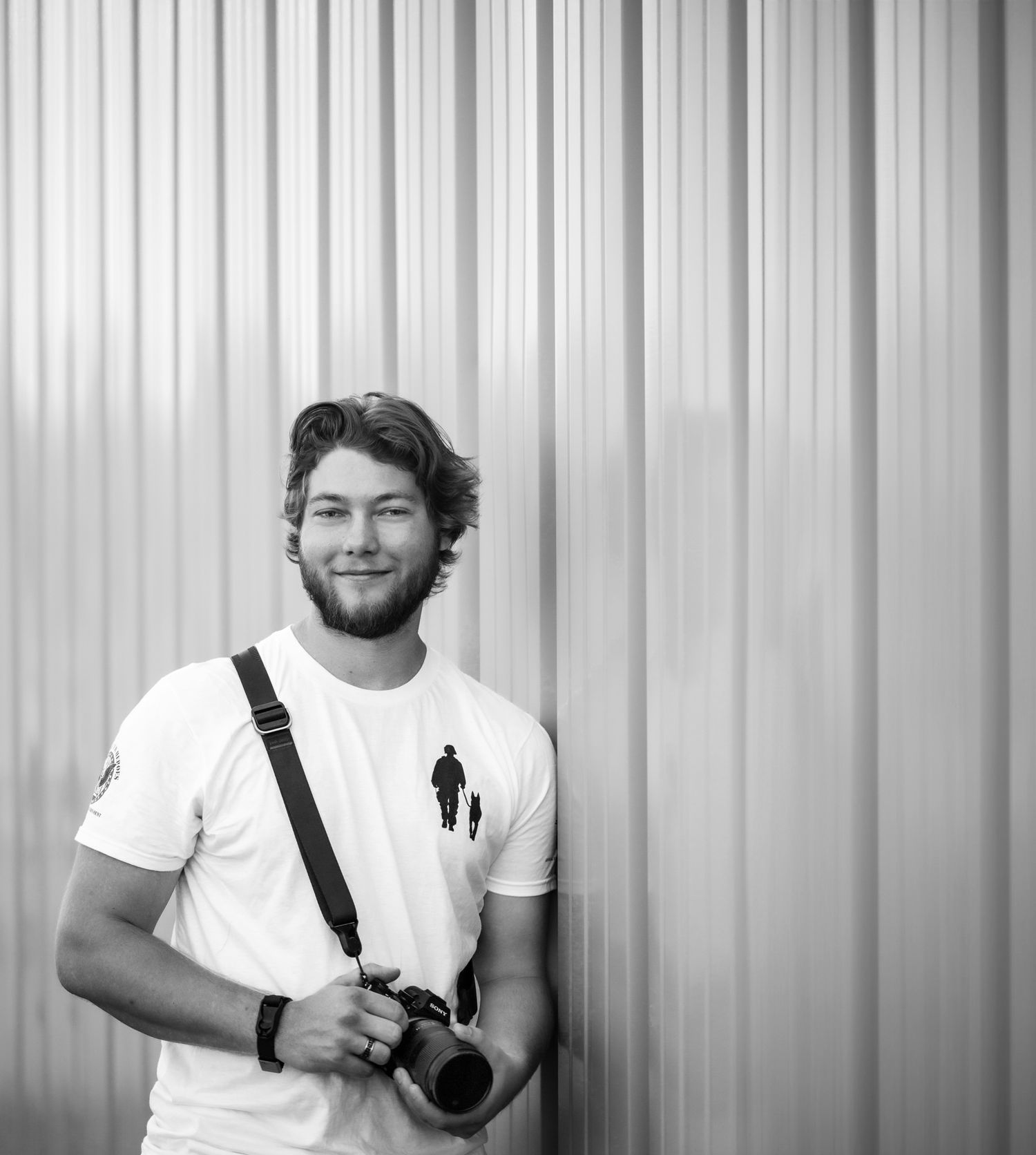 A photographer in a white polo shirt poses against a corrugated wall backdrop.