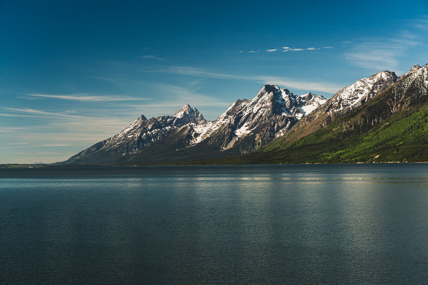Majestic snow-capped mountain range reflected in calm lake waters under blue skies.