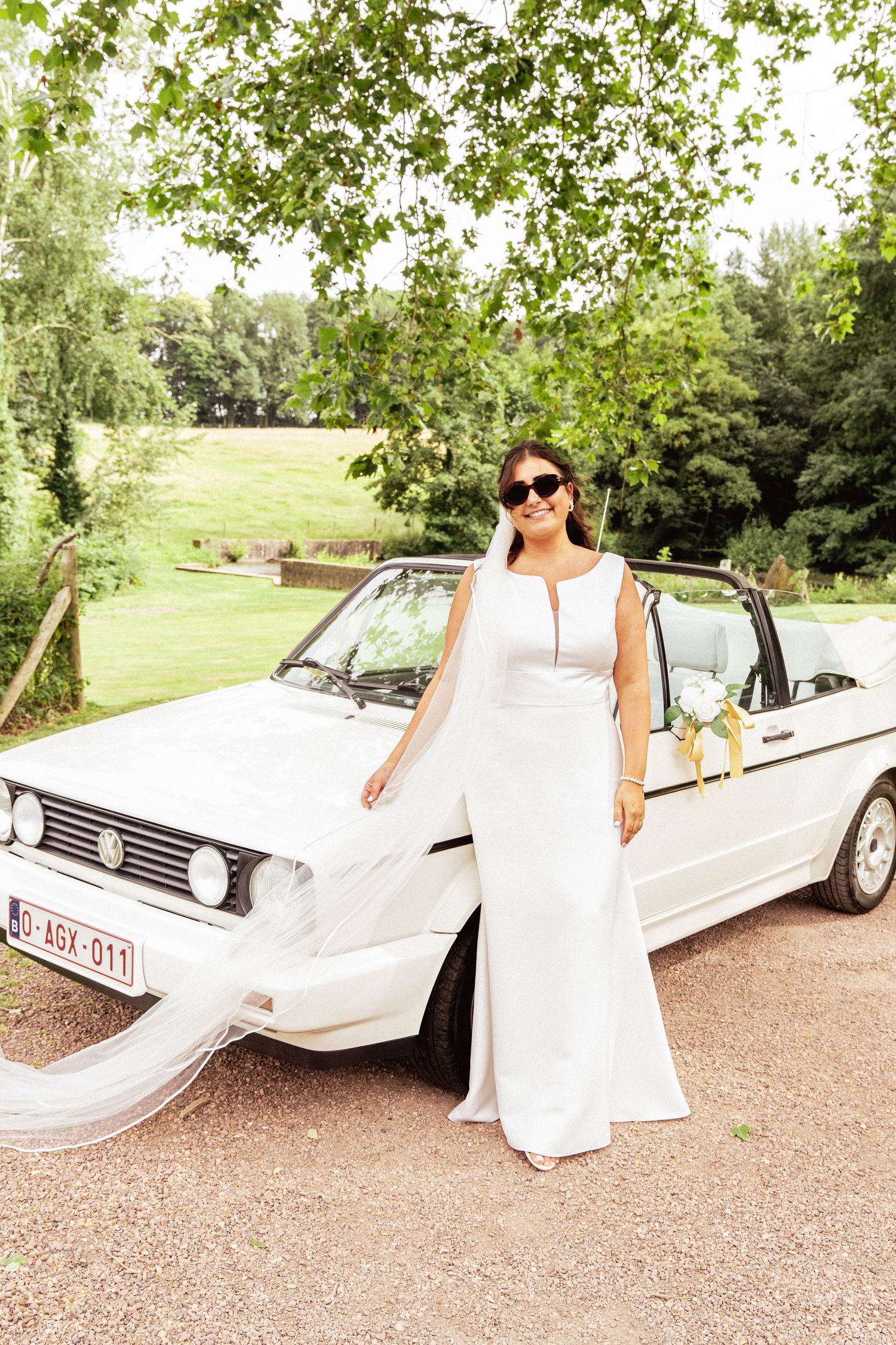 White vintage car parked in lush garden setting with trees and greenery.