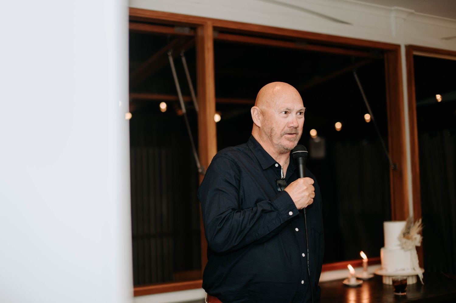 At an evening reception, a speaker addresses guests while holding a microphone.