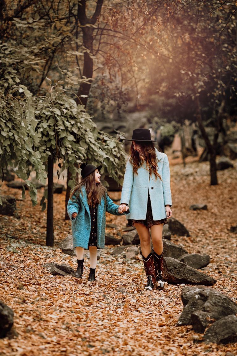 Two people in matching blue coats walking through autumn leaves on a forest path.