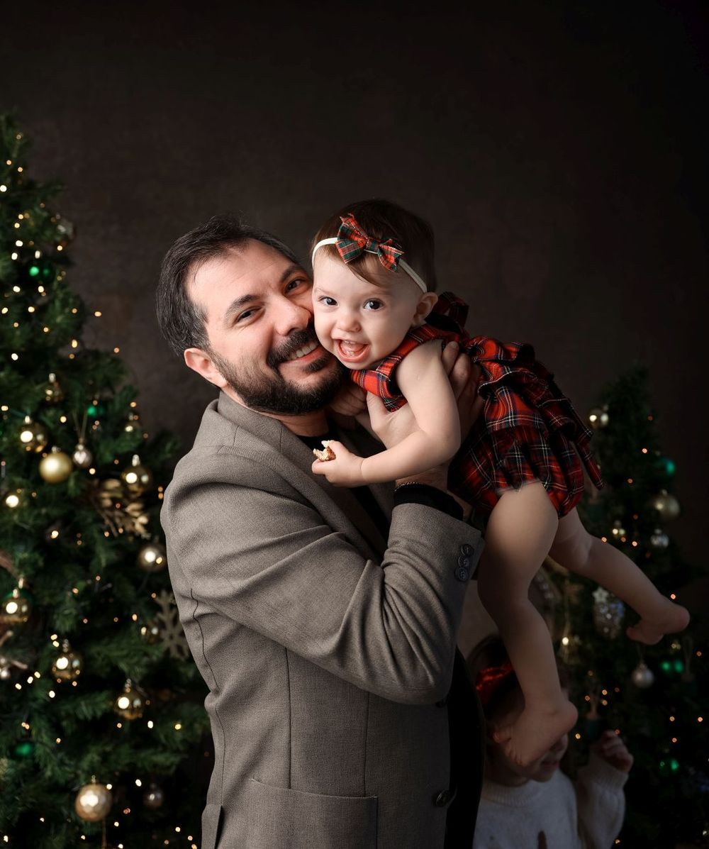 Holiday portrait with decorated Christmas tree and twinkling lights in background.