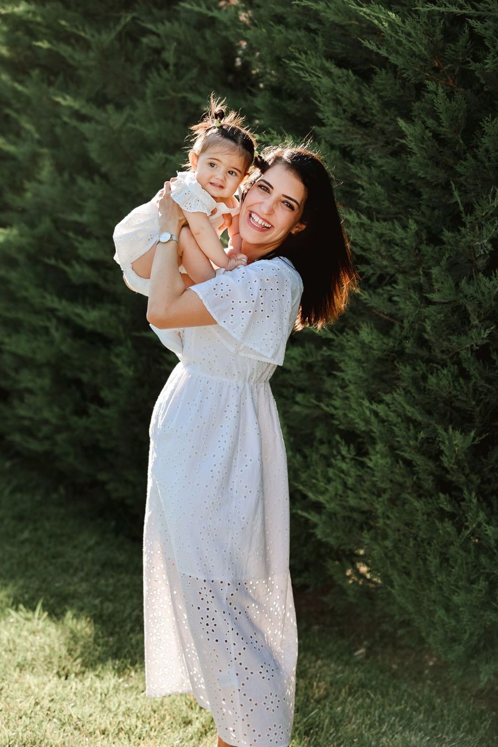 Joy-filled moment shared against green hedge backdrop on sunny day.