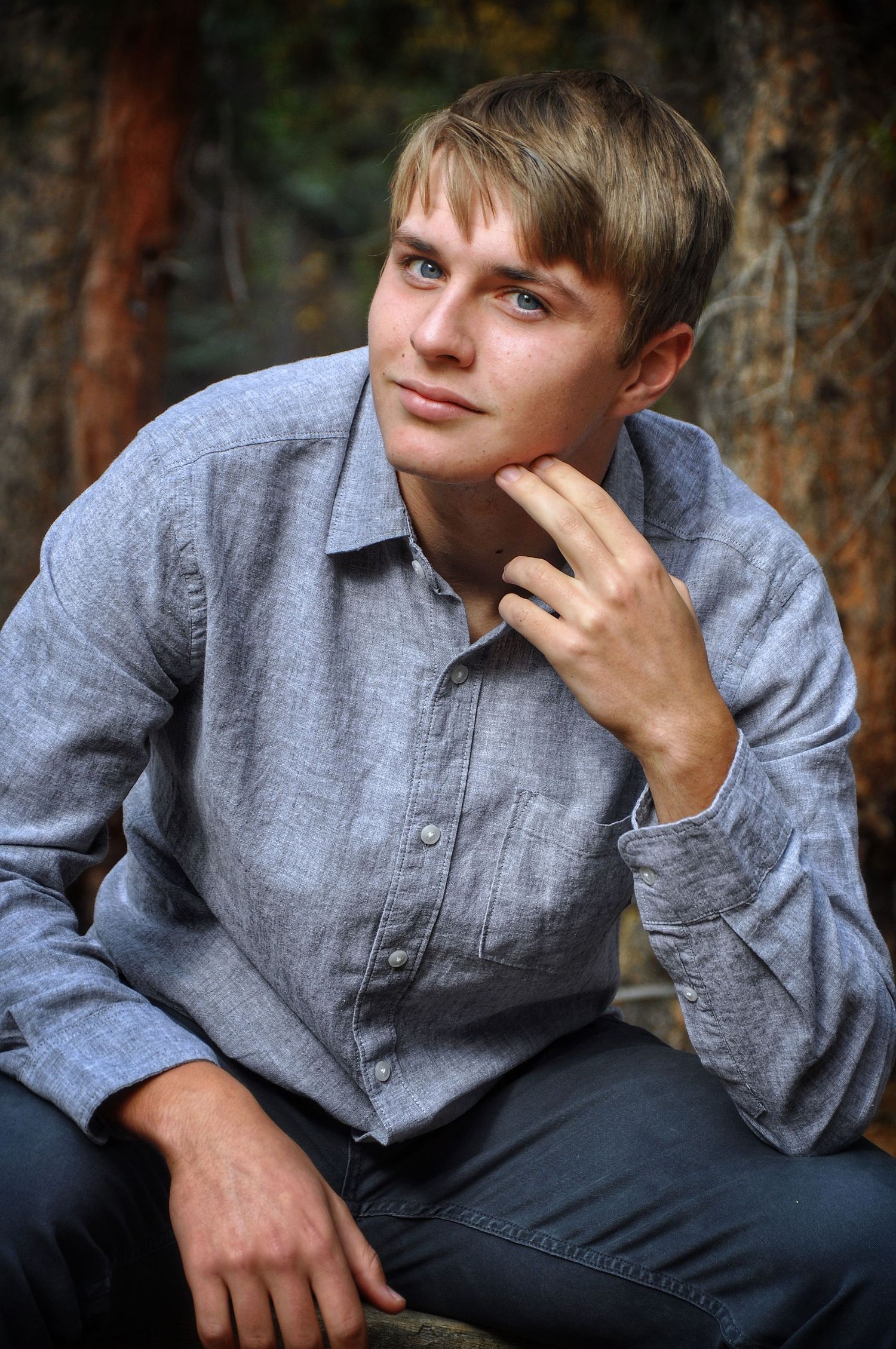 A young man poses in the forest with his hand touching his face.