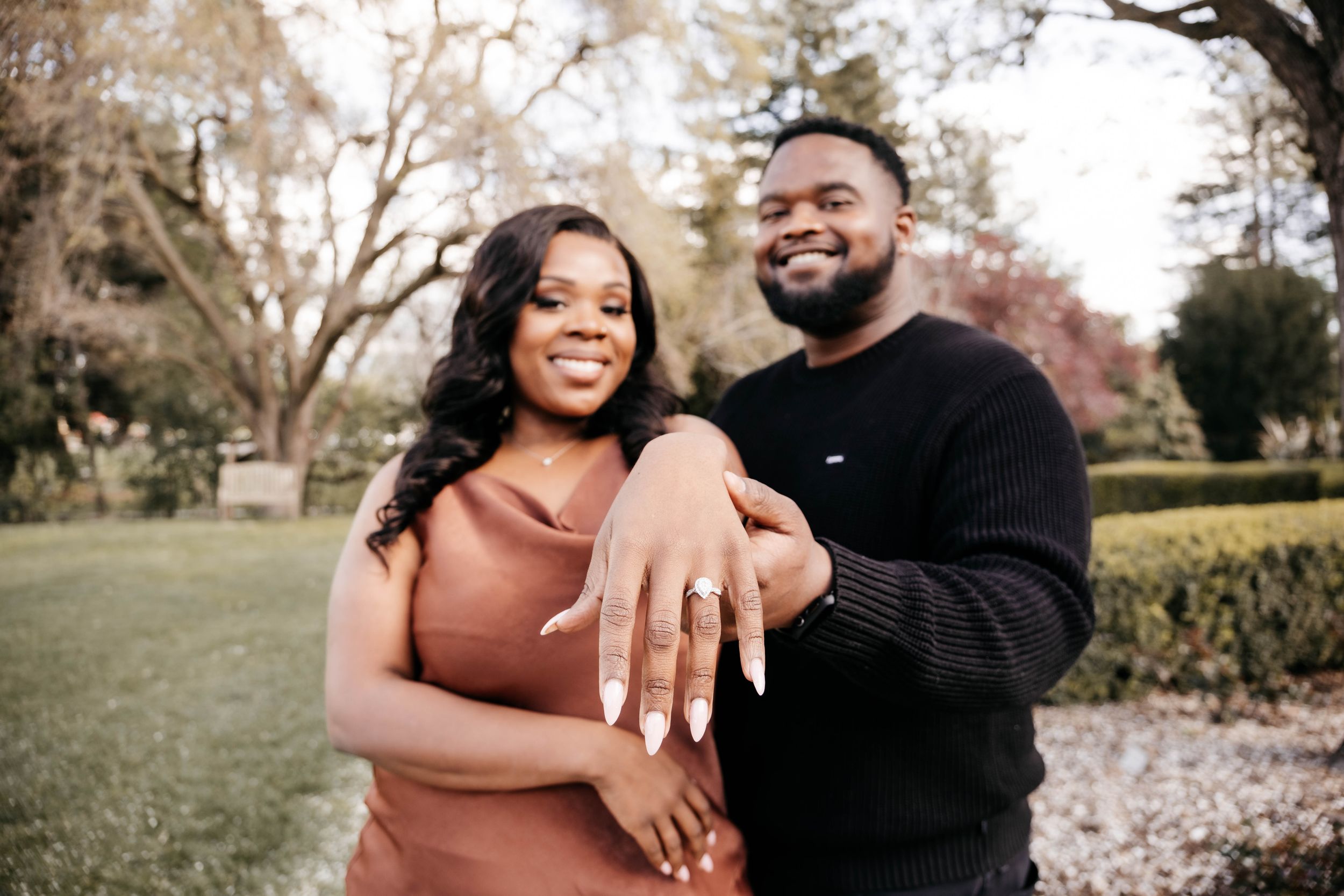 A couple shares tender moments in a garden setting with blooming spring trees in the background.