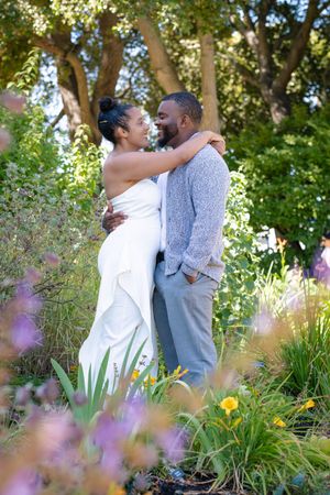 A couple shares an intimate moment in a sunlit garden surrounded by blooming flowers and greenery.