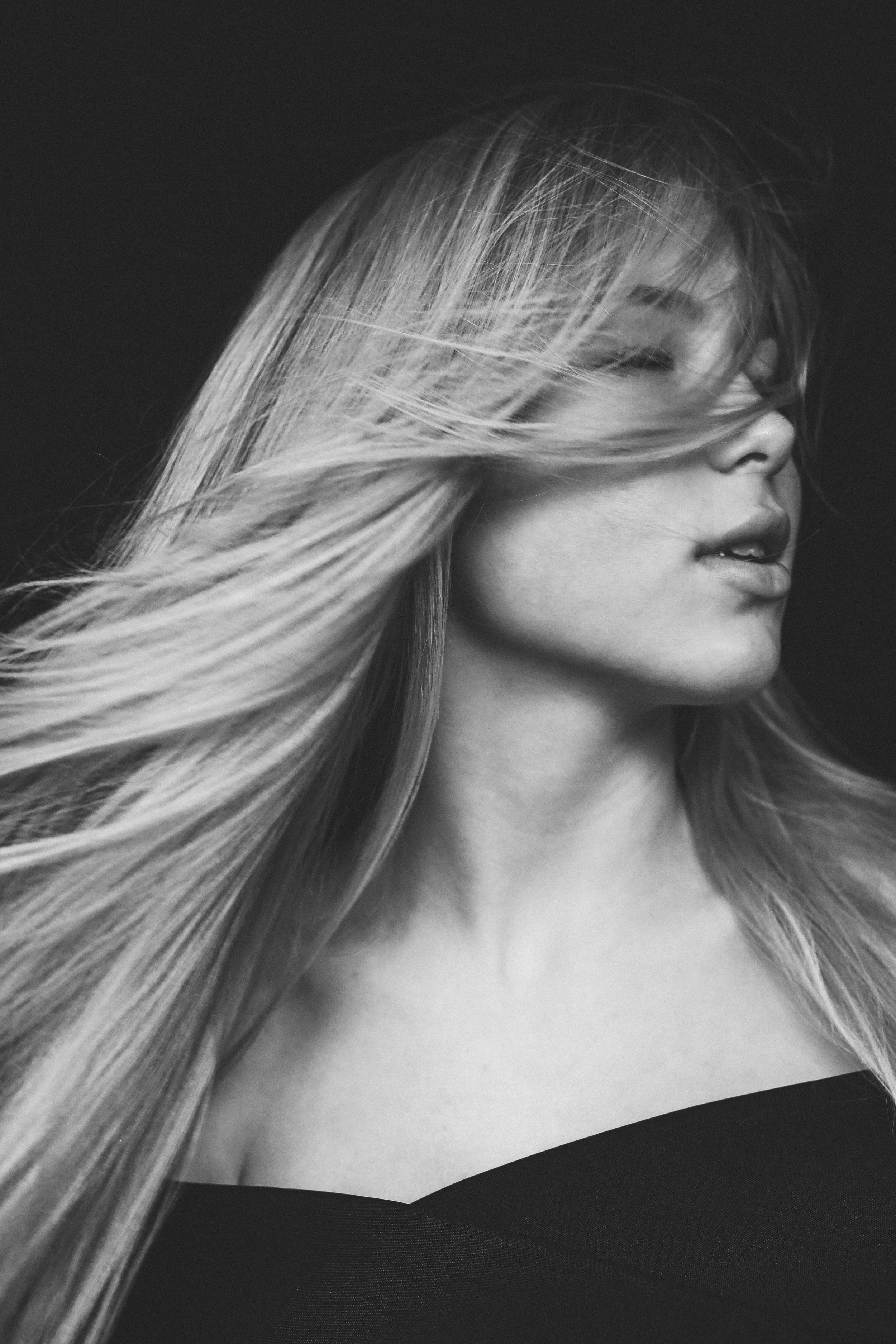 Black and white portrait of a blonde woman with flowing hair covering her eyes against a dark background.