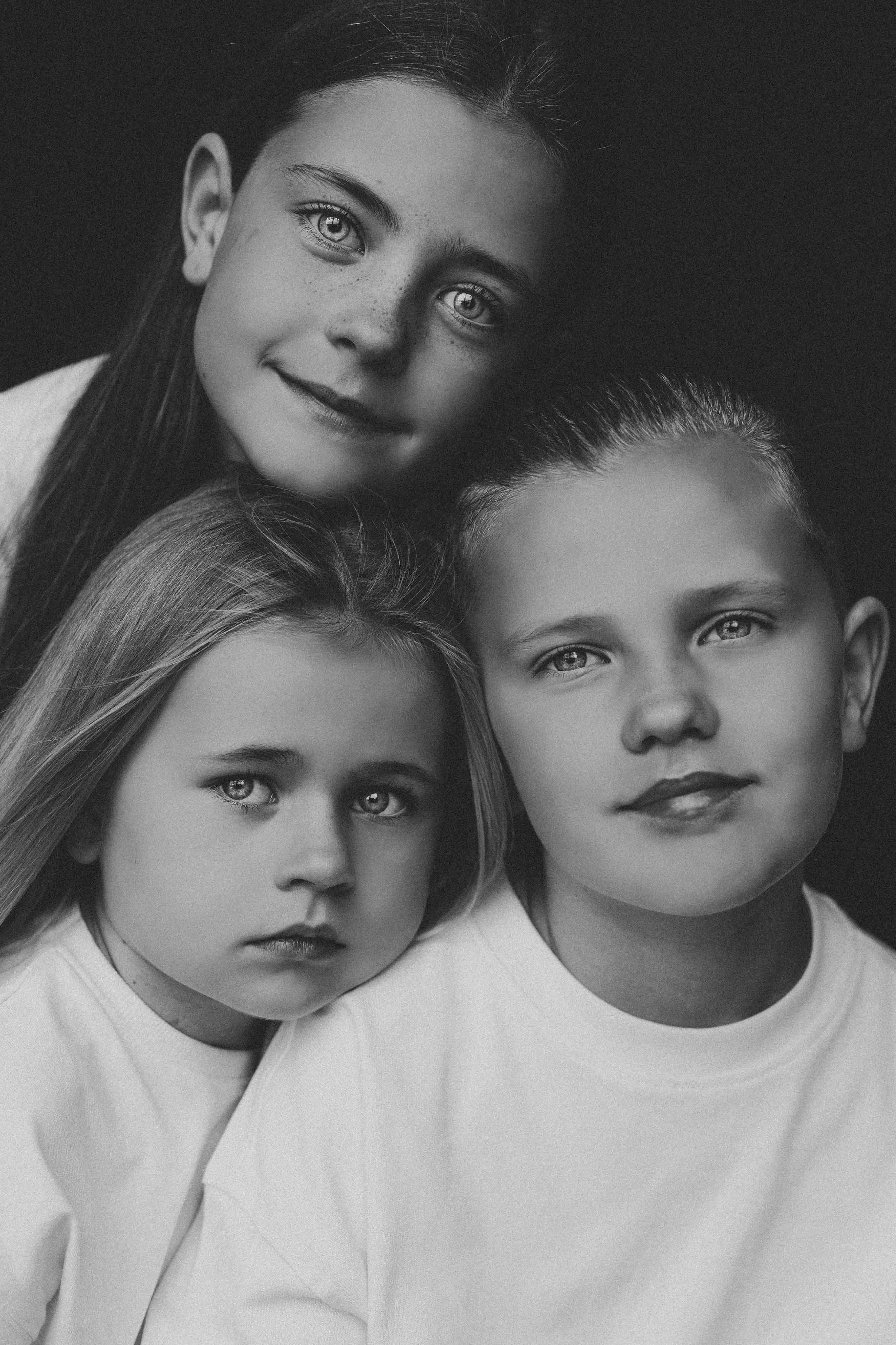 Classic black and white studio portrait of three children in white shirts posing together.