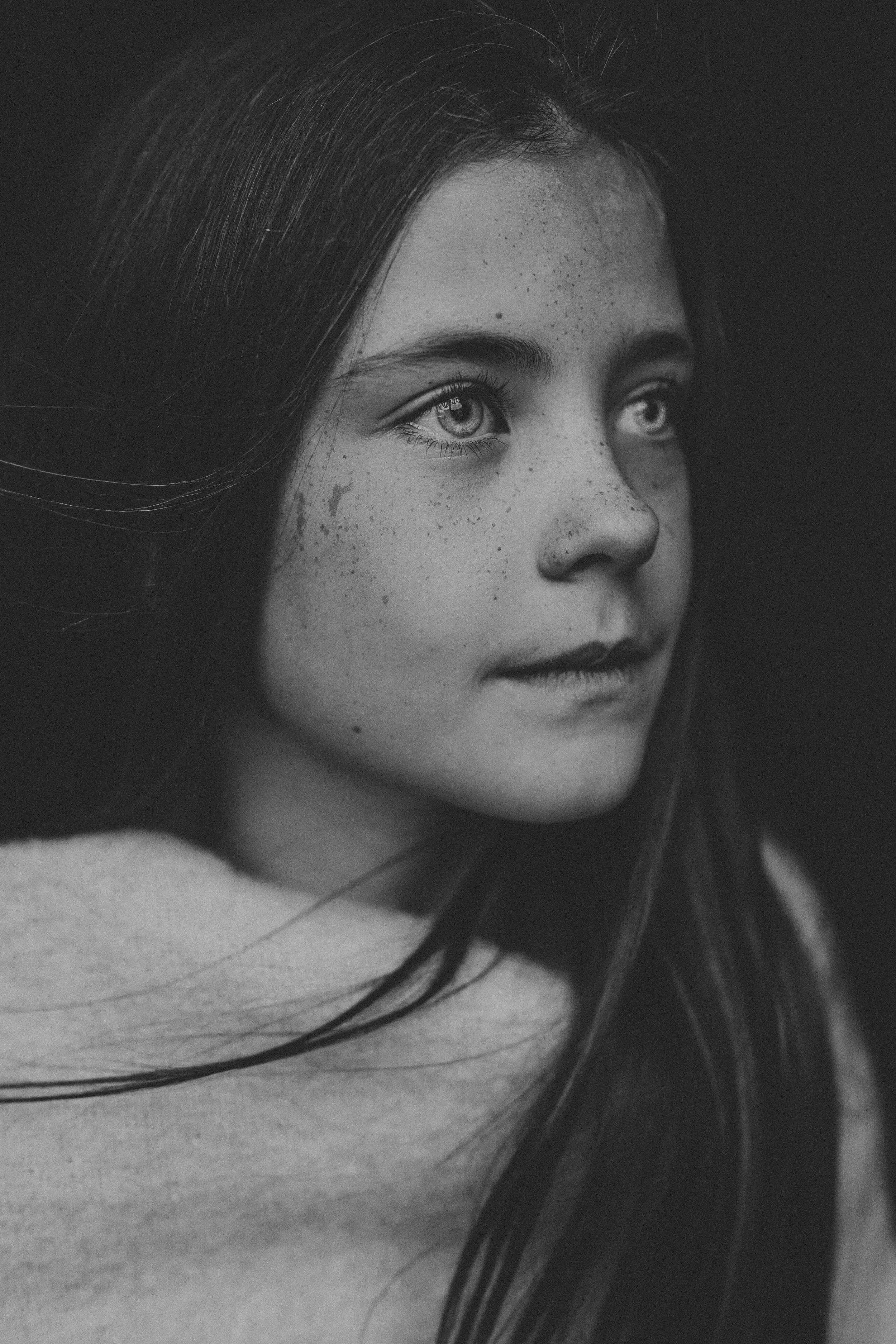 Black and white portrait of a young girl with freckles and long dark hair gazing thoughtfully.