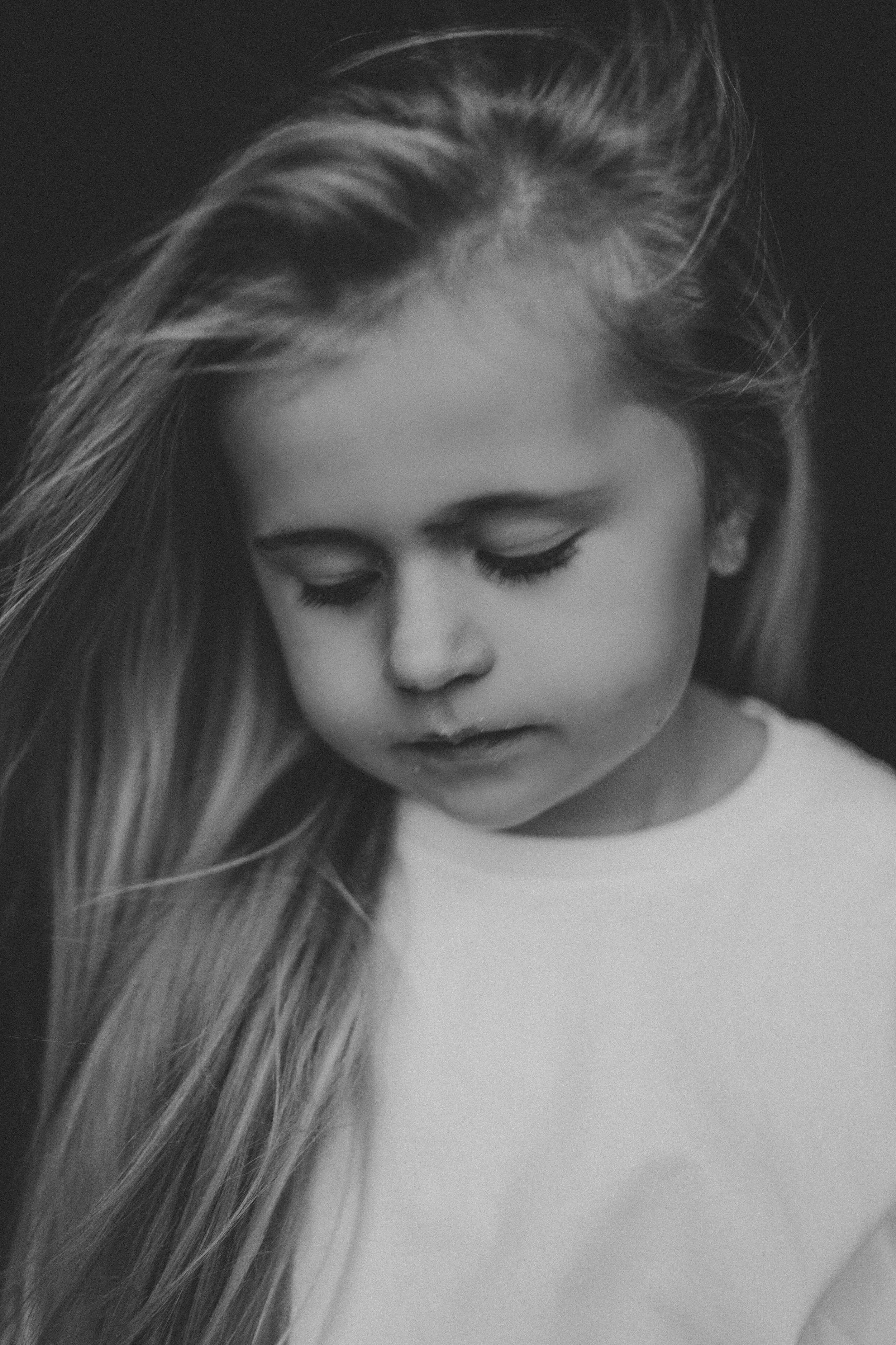 Black and white portrait of a young blonde girl with windswept hair looking down.