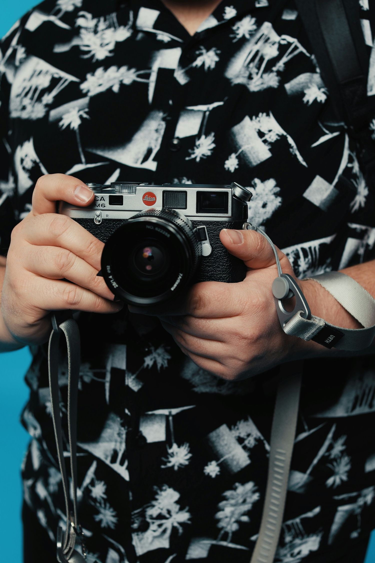 Someone wearing a patterned shirt holds a vintage Leica rangefinder camera with a wide-angle lens.