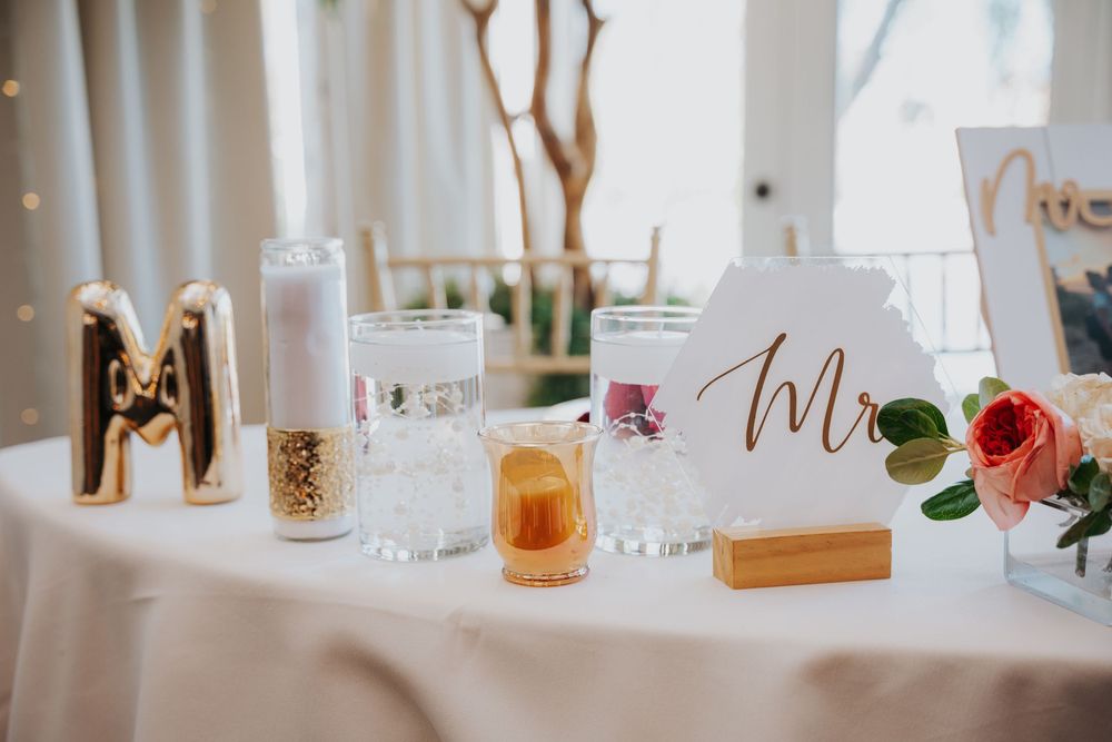 Elegant wedding reception table setting with white linens, floral centerpieces, and golden accents.