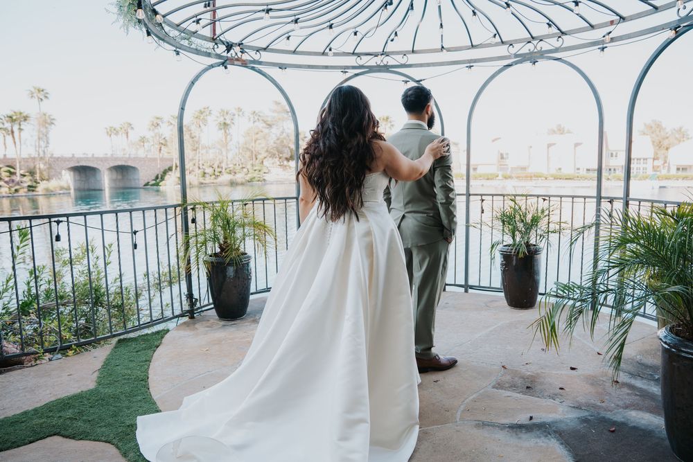 A couple in wedding attire shares a tender moment under a white gazebo with decorative sunburst details.