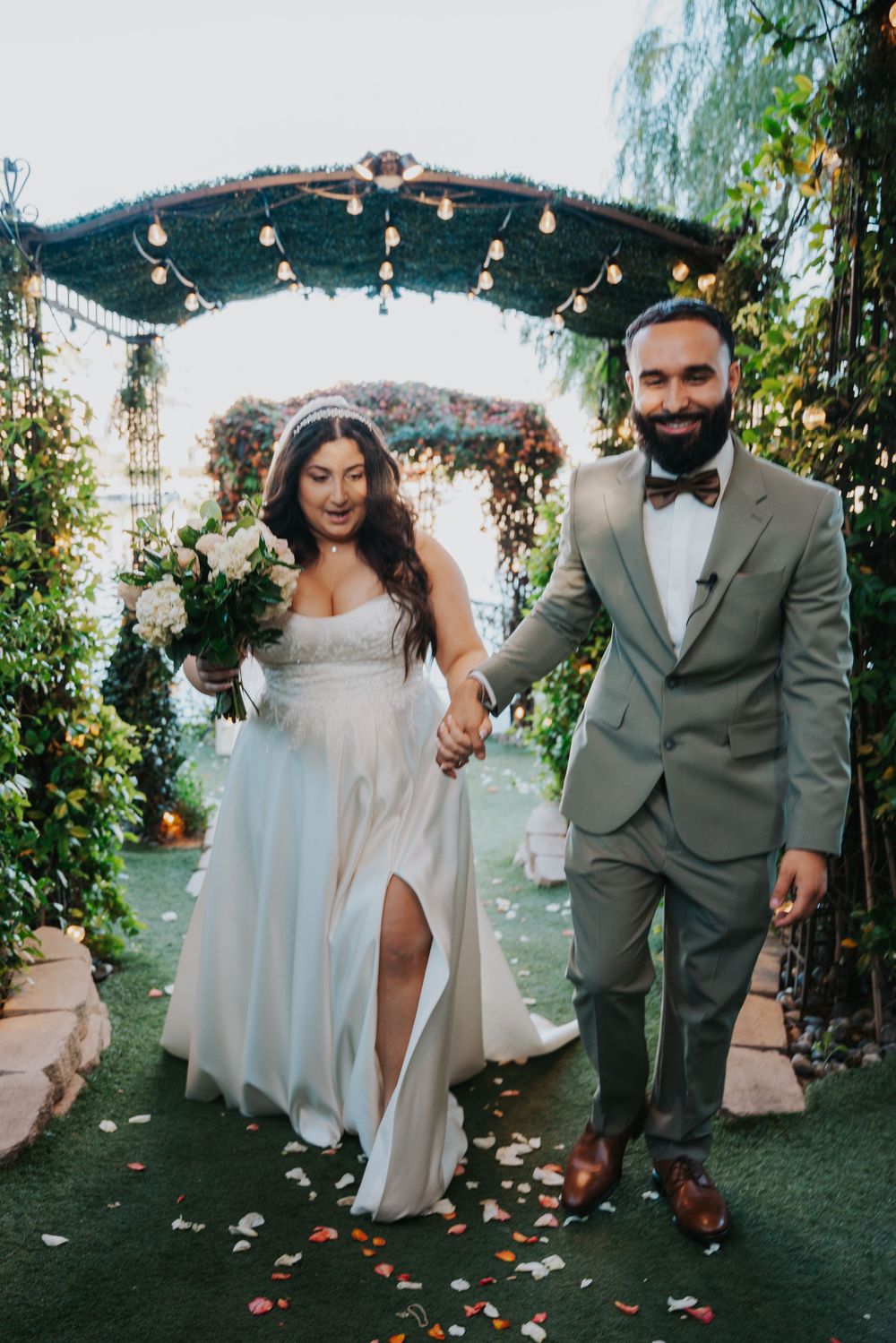 A couple walks and dances together on a garden path decorated with string lights and floral arrangements.