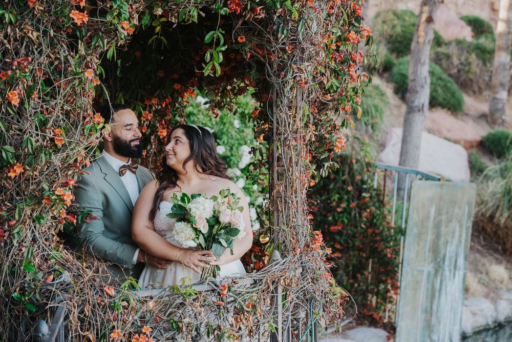 Romantic couple embraces under a blooming orange pyracantha bush in a garden setting.