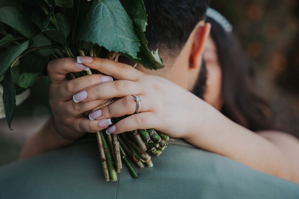 A close-up shot of hands holding a fresh bouquet of flowers with greenery against a blurred background.