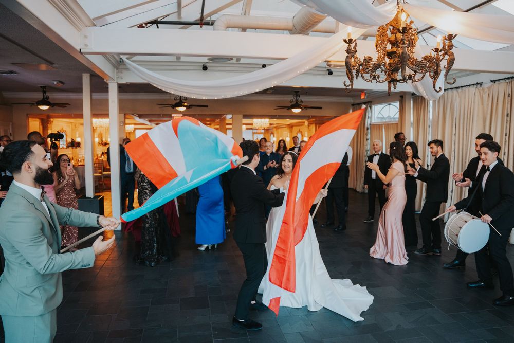 Wedding celebration at an indoor venue with guests waving colorful fabric banners under elegant chandeliers.