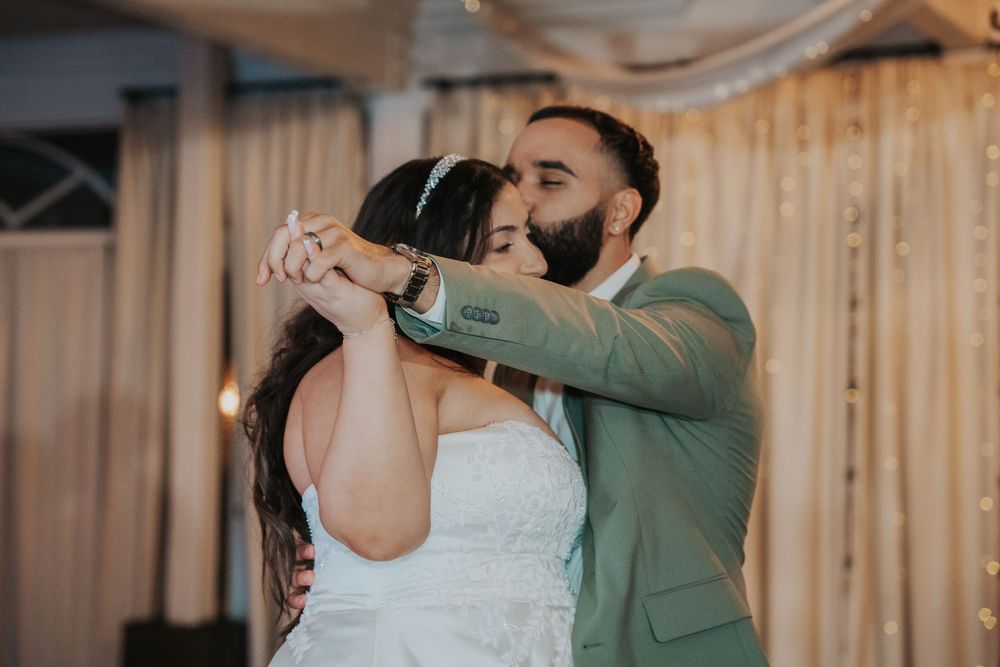 A couple in formal attire dances together at a wedding reception with wooden paneled walls in the background.