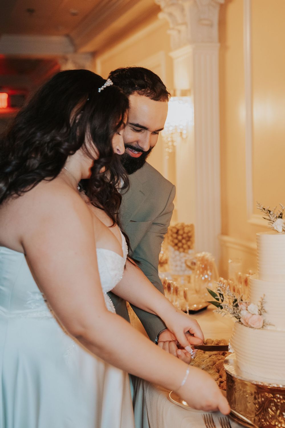 A couple cuts into their elegant white wedding cake during their reception celebration.